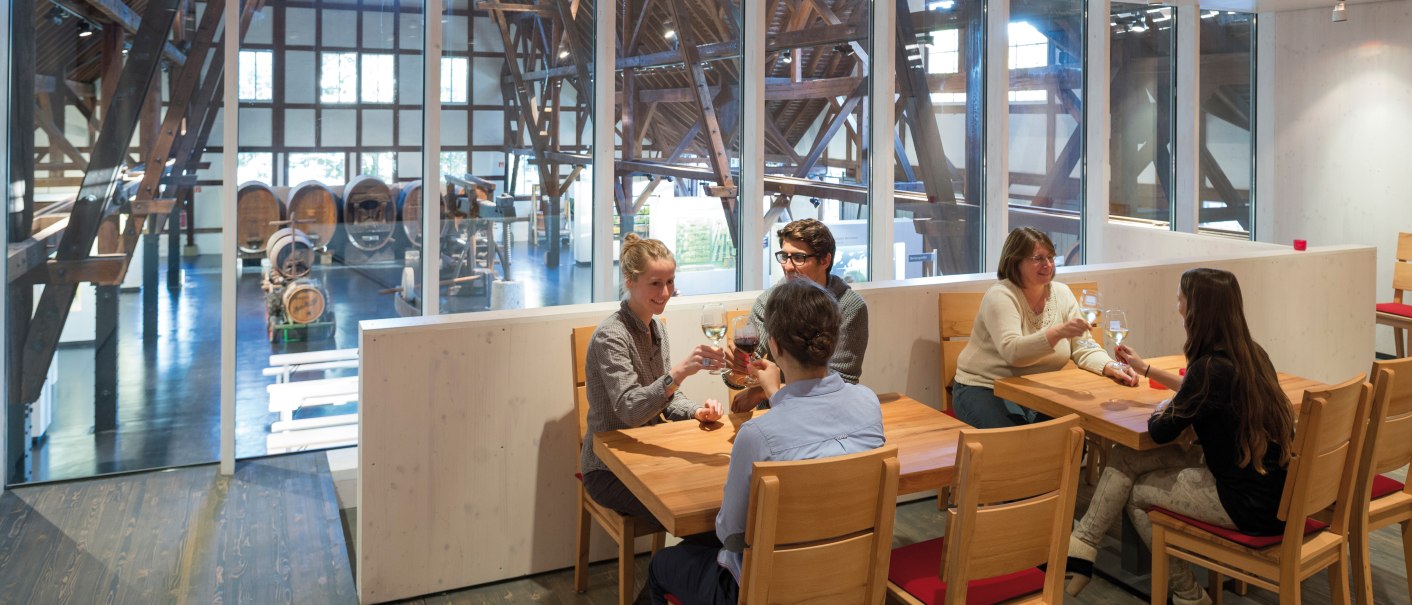 Menschen sitzen in einer modernen Vinothek im Weinbaumuseum Stuttgart, trinken Wein und unterhalten sich. Im Hintergrund sind große Weinfässer sichtbar., © Stuttgart-Marketing GmbH (SMG) Menschen sitzen in einer modernen Vinothek im Weinbaumuseum Stuttgart, trinken Wein und unterhalten sich. Im Hintergrund sind große Weinfässer sichtbar., © Stuttgart-Marketing GmbH (SMG)