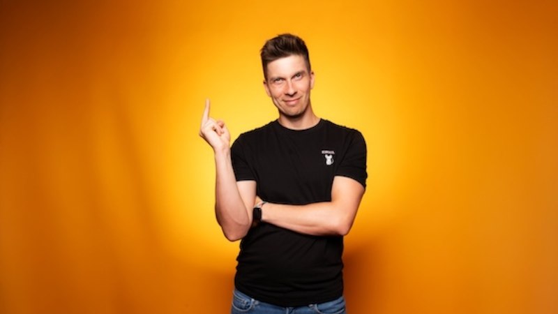 Person in schwarzem T-Shirt und blauer Jeans vor orangefarbenem Hintergrund, zeigt mit Finger nach oben und lächelt leicht., © Renitenztheater Stuttgart e.V. Person in schwarzem T-Shirt und blauer Jeans vor orangefarbenem Hintergrund, zeigt mit Finger nach oben und lächelt leicht., © Renitenztheater Stuttgart e.V.