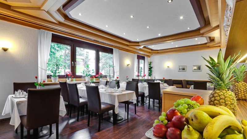 Elegant breakfast room with laid tables, dark chairs and a fruit bowl in the foreground. Large windows let in plenty of light., © ARNOTEL GmbH