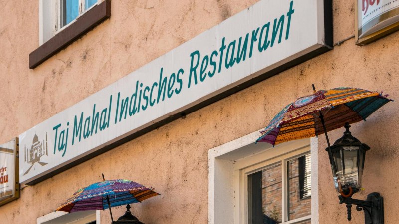 Fassade eines indischen Restaurants in Stuttgart mit bunten Schirmen und einem Schild mit der Aufschrift 'Taj Mahal Indisches Restaurant'., &copy; SMG, Sarah Schmid