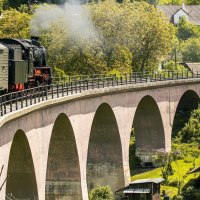 A steam locomotive pulls a train across a bridge in a green, rural landscape. People are looking out the windows and taking pictures., &copy; SMG Stuttgart Marketing GmbH - Sarah Schmid