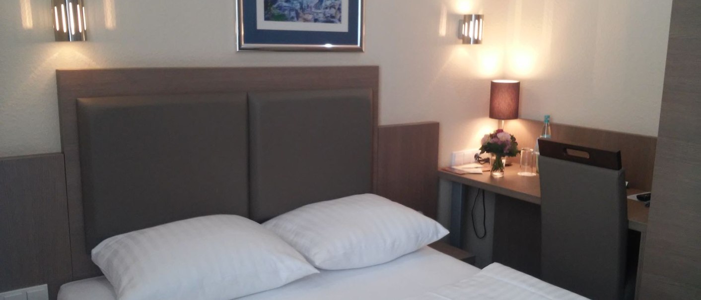 Ein gemütliches Hotelzimmer mit Queensize-Bett, Schreibtisch, Wandlampen und einem Bild an der Wand., © Novum Boulevard Stuttgart City Ein gemütliches Hotelzimmer mit Queensize-Bett, Schreibtisch, Wandlampen und einem Bild an der Wand., © Novum Boulevard Stuttgart City