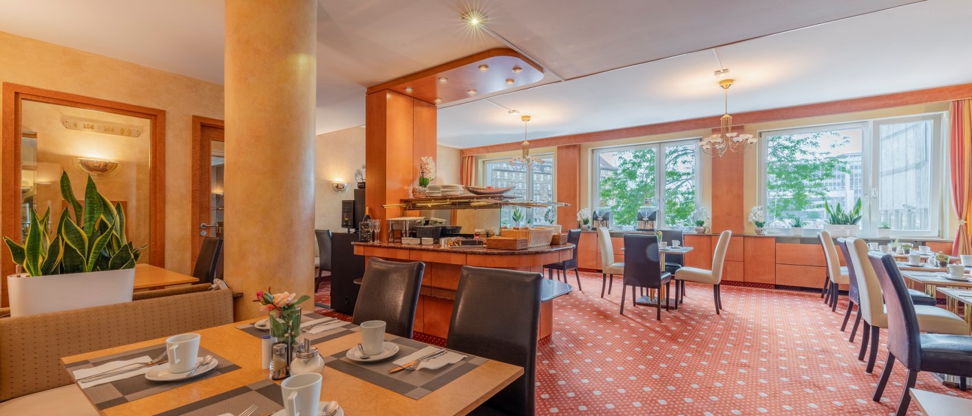 Elegant breakfast room with laid tables, plants and large windows. Warm colors and cozy atmosphere., © PLAZA INN Rieker Stuttgart Hauptbahnhof