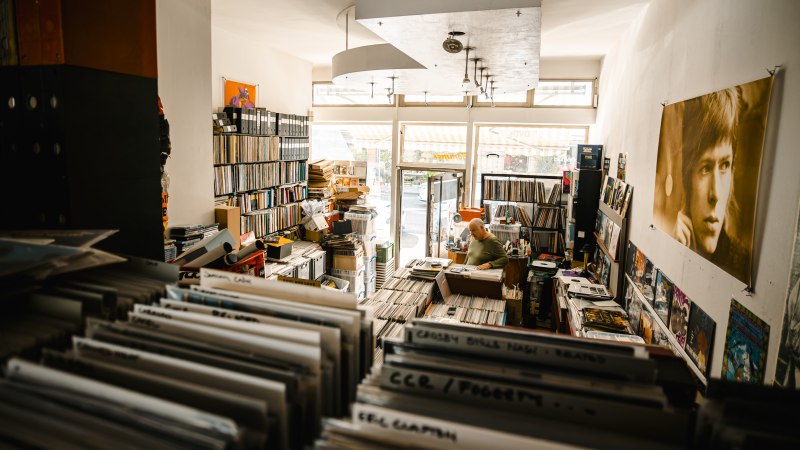 A cozy record store full of records. A man sits at a desk, surrounded by shelves and posters on the walls., © SMG Stuttgart Marketing GmbH - Sarah Schmid A cozy record store full of records. A man sits at a desk, surrounded by shelves and posters on the walls., © SMG Stuttgart Marketing GmbH - Sarah Schmid