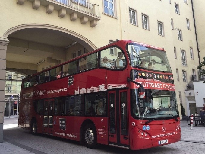 Roter Doppeldeckerbus der Stuttgart Citytour fährt durch einen Torbogen in einer städtischen Umgebung., © Willms Touristik Roter Doppeldeckerbus der Stuttgart Citytour fährt durch einen Torbogen in einer städtischen Umgebung., © Willms Touristik