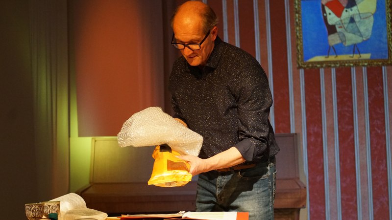 Ein Mann mit Brille packt ein gelbes Paket in Luftpolsterfolie ein. Er steht an einem Tisch, im Hintergrund ein buntes Bild an der Wand., &copy; Katja Ritter