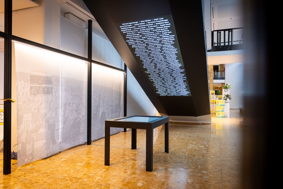 Rauminstallation im Stuttgarter Rathaus mit projizierten Namen an der Decke und einem interaktiven Tisch auf einem glänzenden Boden., © Julian Rettig Rauminstallation im Stuttgarter Rathaus mit projizierten Namen an der Decke und einem interaktiven Tisch auf einem glänzenden Boden., © Julian Rettig