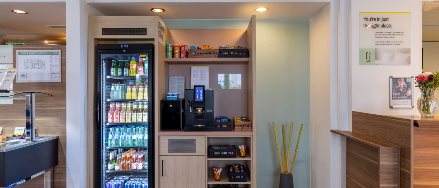 A modern reception area with a refrigerator stocked with beverages and a shelf with snacks. A coffee machine is available., &copy; Novum  Hospitality