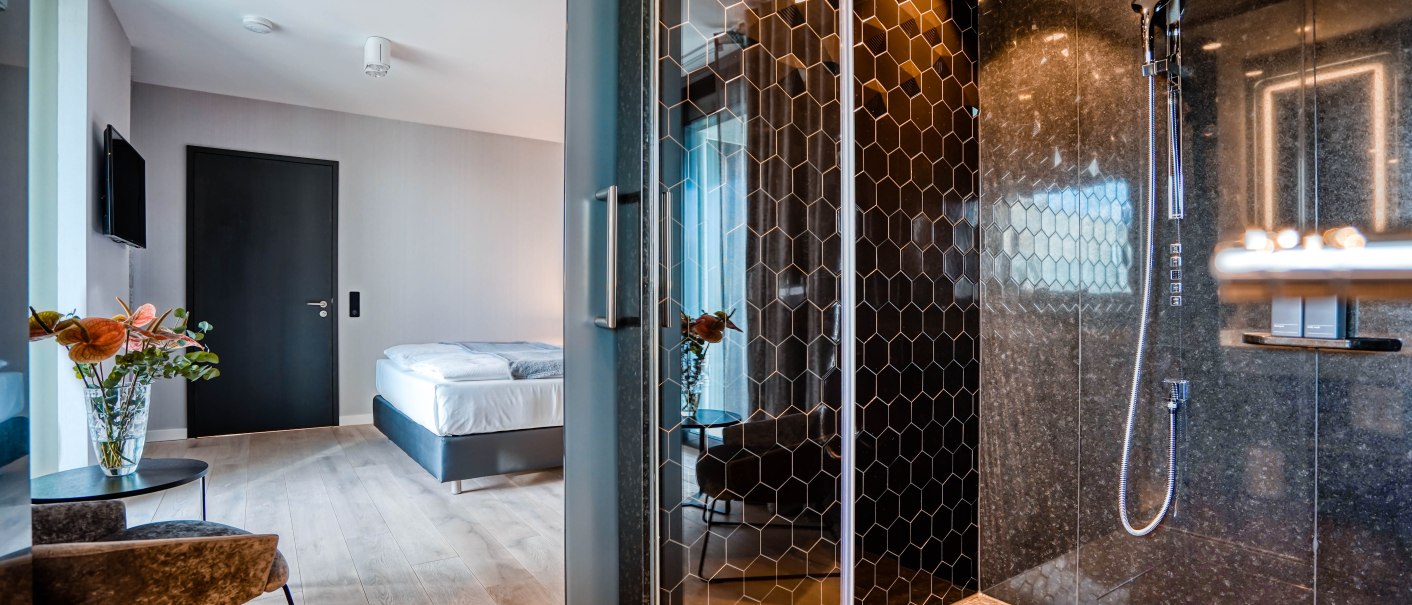 Moderne Hotelsuite mit elegantem Design, Bett, Glasdusche mit Wabenmuster, Blumen und stilvollen Möbeln auf Holzboden., © CLOUD N°7 APARTMENTS GmbH Moderne Hotelsuite mit elegantem Design, Bett, Glasdusche mit Wabenmuster, Blumen und stilvollen Möbeln auf Holzboden., © CLOUD N°7 APARTMENTS GmbH