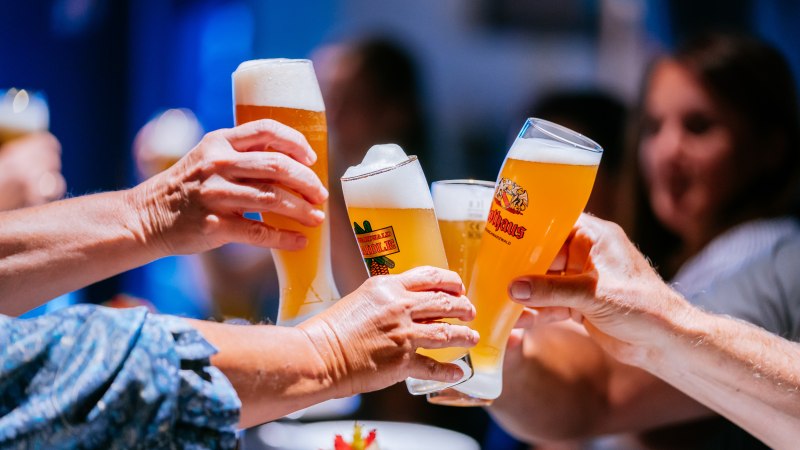 Mehrere Personen stoßen mit gefüllten Biergläsern an, im Hintergrund sind unscharf weitere Personen zu sehen., © Stuttgart-Marketing GmbH, Thomas Niedermüller