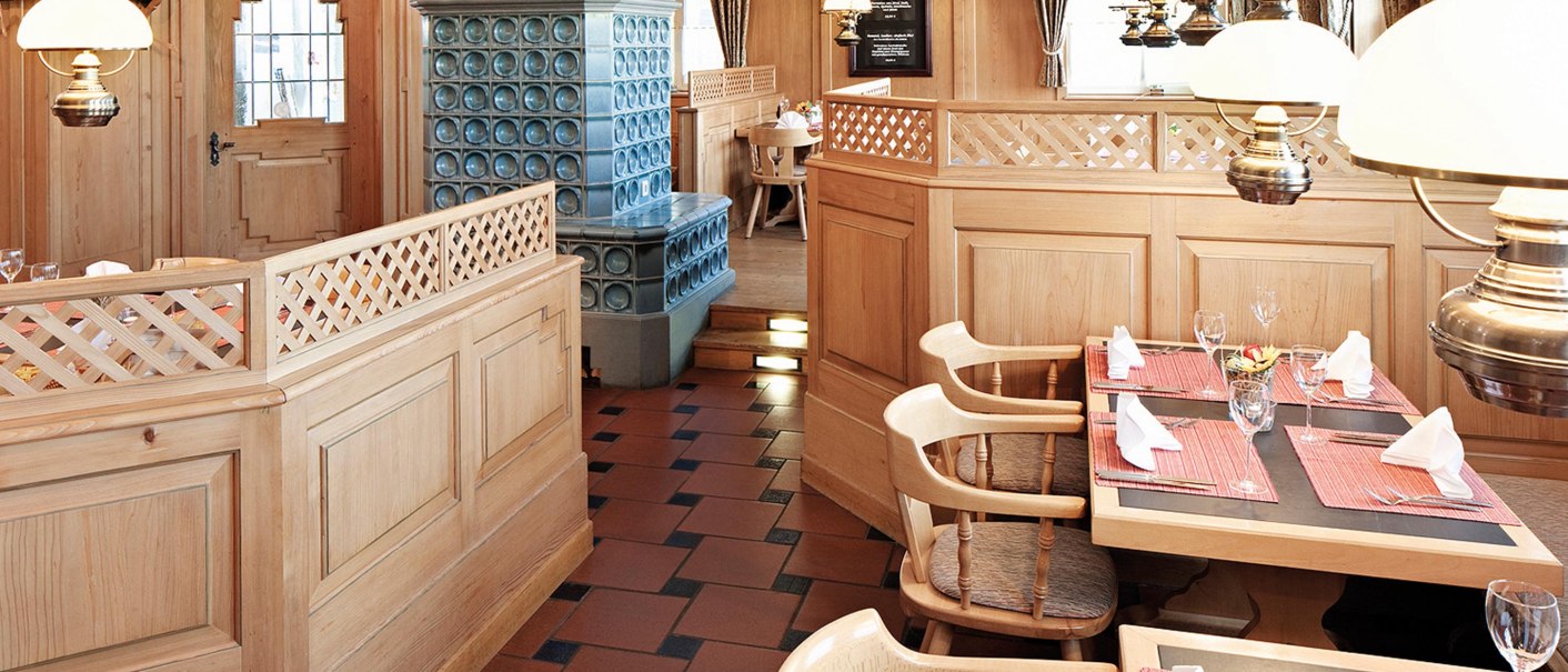 Gem&uuml;tliches Restaurant mit Holzm&ouml;beln, Kachelofen und dekorativen Lampen. Tische sind mit roten Platzdeckchen und gefalteten Servietten gedeckt., &copy; Seminaris Hotel Bad Boll