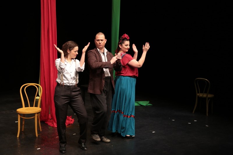 Three people in theater costumes are standing on a stage. Two chairs can be seen in the background. The scene looks dramatic and lively., &copy; tri-b&uuml;hne e.V.