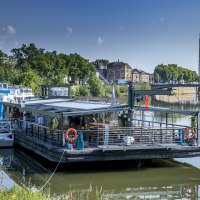 A floating restaurant on the Neckar, surrounded by green vegetation and urban buildings in the background., © all copyrights are reserved by maks richter