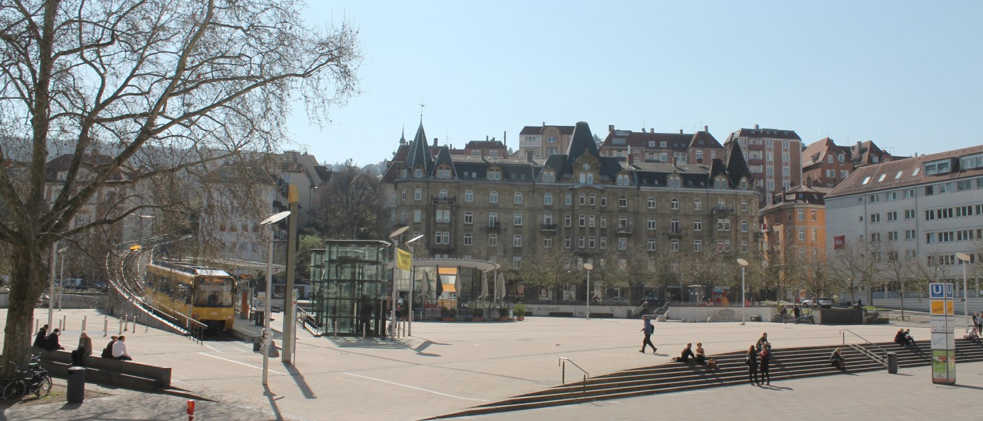 Marienplatz in Stuttgart with streetcar, modern and historic buildings. People sitting on steps, trees without leaves, sunny day., © Stuttgart-Marketing GmbH Marienplatz in Stuttgart with streetcar, modern and historic buildings. People sitting on steps, trees without leaves, sunny day., © Stuttgart-Marketing GmbH