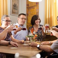 A group of people sit at a table and toast with drinks. They look cheerful and relaxed. There are yellow curtains in the background., &copy; Stuttgart-Marketing GmbH / Winkler