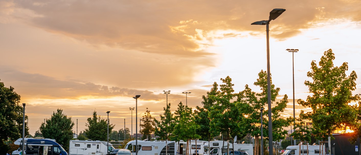 Wohnmobilstellplatz in Fellbach bei Sonnenuntergang. Mehrere Wohnmobile und Autos sind geparkt, umgeben von Bäumen und Straßenlaternen., © Stuttgart-Marketing GmbH, Thomas Niedermüller Wohnmobilstellplatz in Fellbach bei Sonnenuntergang. Mehrere Wohnmobile und Autos sind geparkt, umgeben von Bäumen und Straßenlaternen., © Stuttgart-Marketing GmbH, Thomas Niedermüller