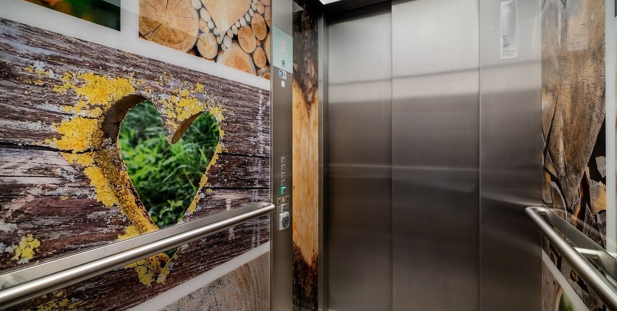 Ein Fahrstuhl mit Holzmuster und Herzmotiven an den Wänden. Die Türen sind aus Metall, und es gibt Handläufe an den Seiten., © Novum Hospitality