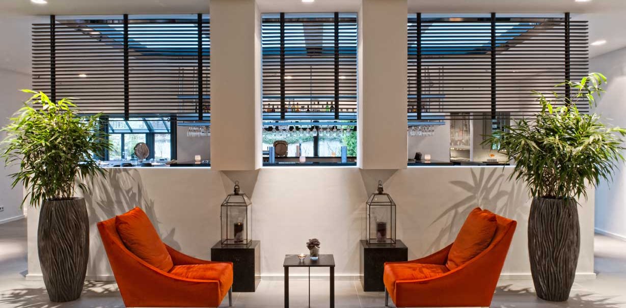 Modern lobby with two orange armchairs, large plants in vases and decorative lanterns on black tables., &copy; Wyndham Stuttgart Airport Messe