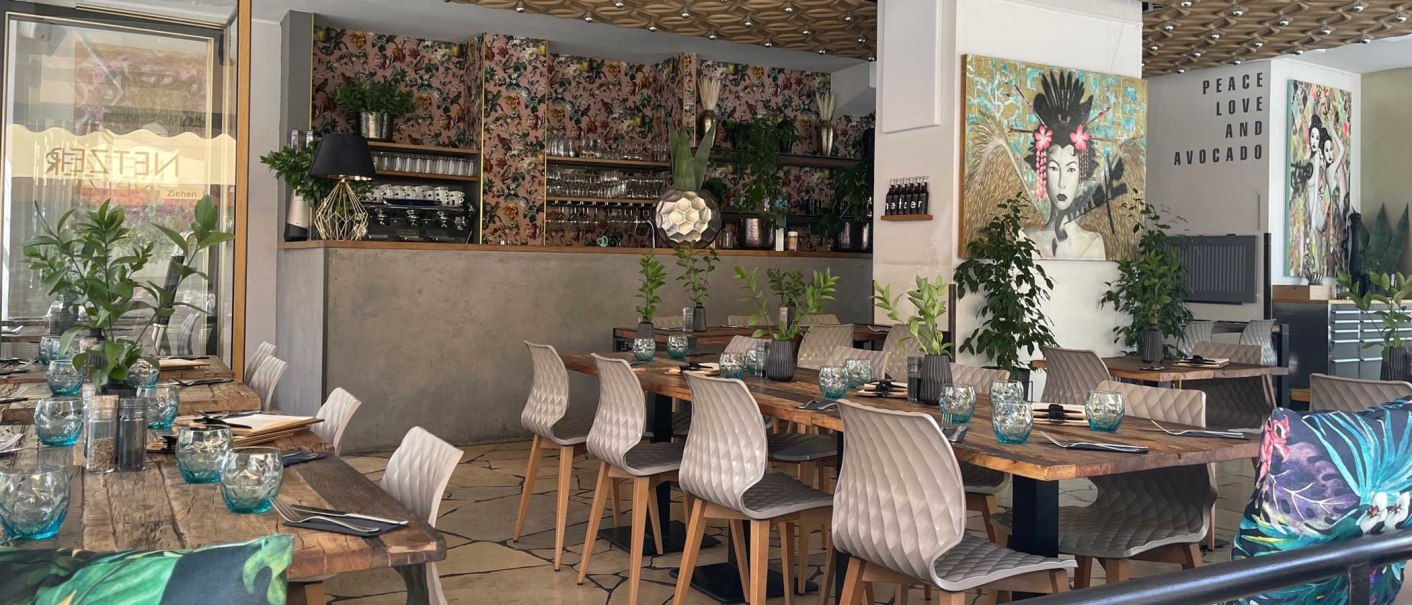Stylishly furnished restaurant with wooden tables, modern chairs, plants and works of art. "Peace Love and Avocado" lettering on the wall., © SMG