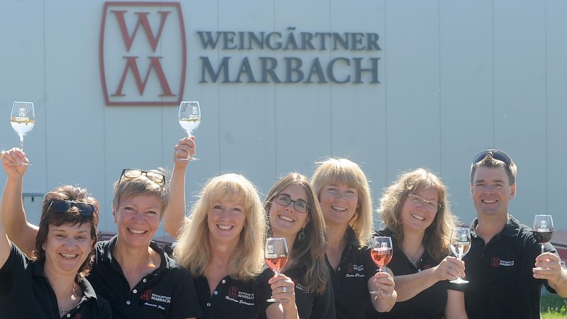 Sieben Personen heben lächelnd Weingläser vor einem Gebäude mit 'Weingärtner Marbach'-Logo., © Weingärtner Marbach e. G.