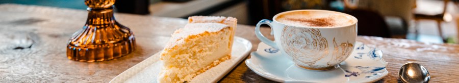 Ein St&uuml;ck Kuchen und eine Tasse Kaffee auf einem Holztisch in einem gem&uuml;tlichen Caf&eacute;. Im Hintergrund unscharfe M&ouml;bel., &copy; Stuttgart-Marketing GmbH, Sarah Schmid