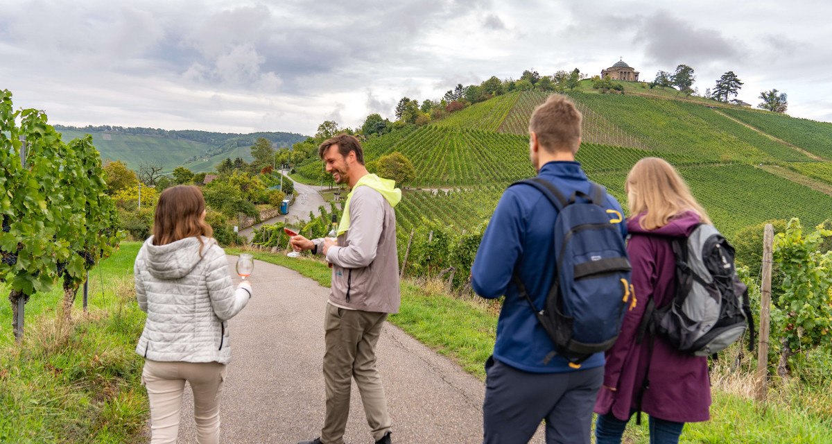 People walking along a wine trail, holding wine glasses. Vineyards and the burial chapel on a hill in the background., &copy; Stuttgart-Marketing GmbH, Martina Denker