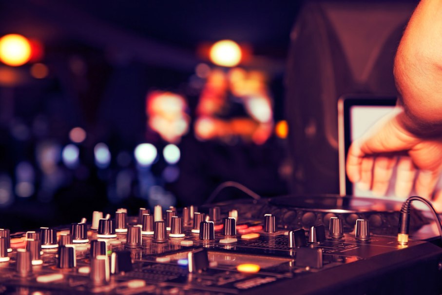 A DJ mixer with lots of controls and a hand operating it. Colorful lights and blurred shapes can be seen in the background., © Planetarium Stuttgart A DJ mixer with lots of controls and a hand operating it. Colorful lights and blurred shapes can be seen in the background., © Planetarium Stuttgart