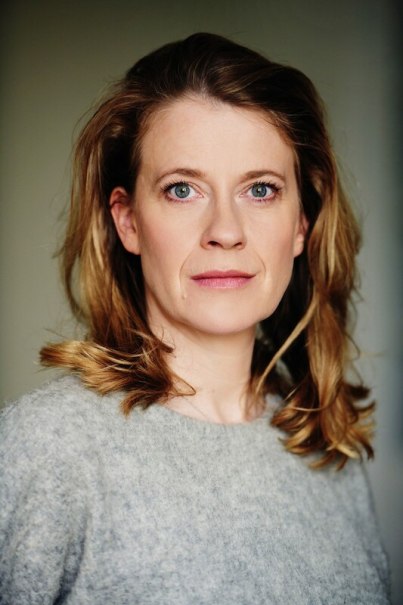 A woman with blonde hair and a gray sweater looks directly into the camera. The background is neutral., &copy; Theaterhaus Stuttgart e.V.