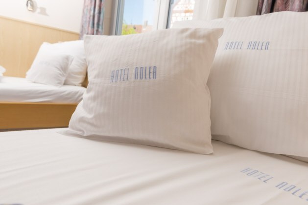Weiße Kissen und Bettwäsche mit 'Hotel Adler'-Aufdruck in einem hellen Hotelzimmer., © Hotel Adler Waiblingen Weiße Kissen und Bettwäsche mit 'Hotel Adler'-Aufdruck in einem hellen Hotelzimmer., © Hotel Adler Waiblingen