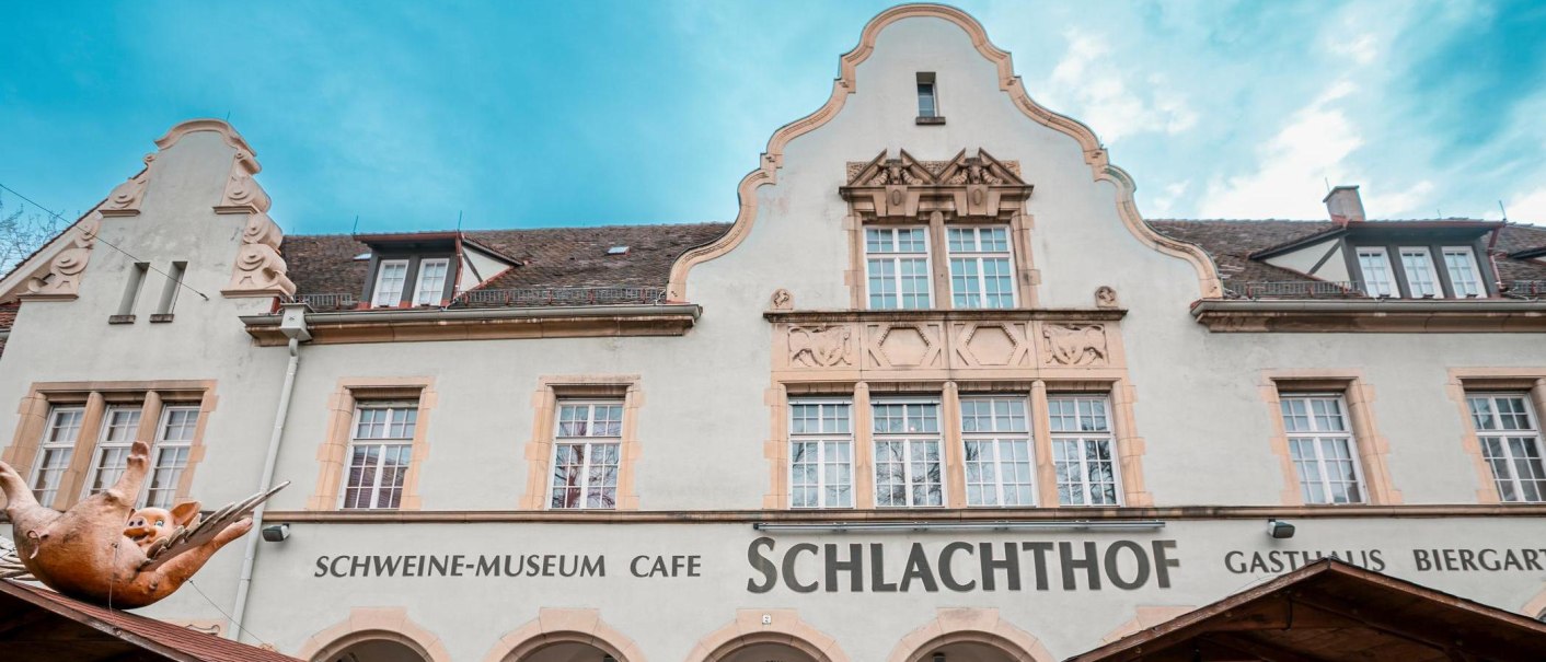Fassade des Schweinemuseums in Stuttgart mit dem Schriftzug 'Schlachthof' und einer Schweinskulptur auf dem Dach., © Stuttgart-Marketing GmbH, Sarah Schmid Fassade des Schweinemuseums in Stuttgart mit dem Schriftzug 'Schlachthof' und einer Schweinskulptur auf dem Dach., © Stuttgart-Marketing GmbH, Sarah Schmid