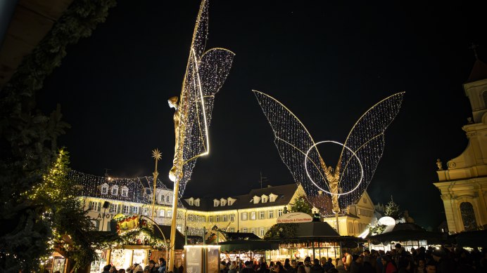 Der Ludwigsburger Barock-Weihnachtsmarkt auf dem Marktplatz bei Nacht, beleuchtete große Engelsfiguren und Buden. Einige Besucherinnen und Besucher tummeln sich auf dem Platz., © Stuttgart Marketing GmbH, Sarah Schmid