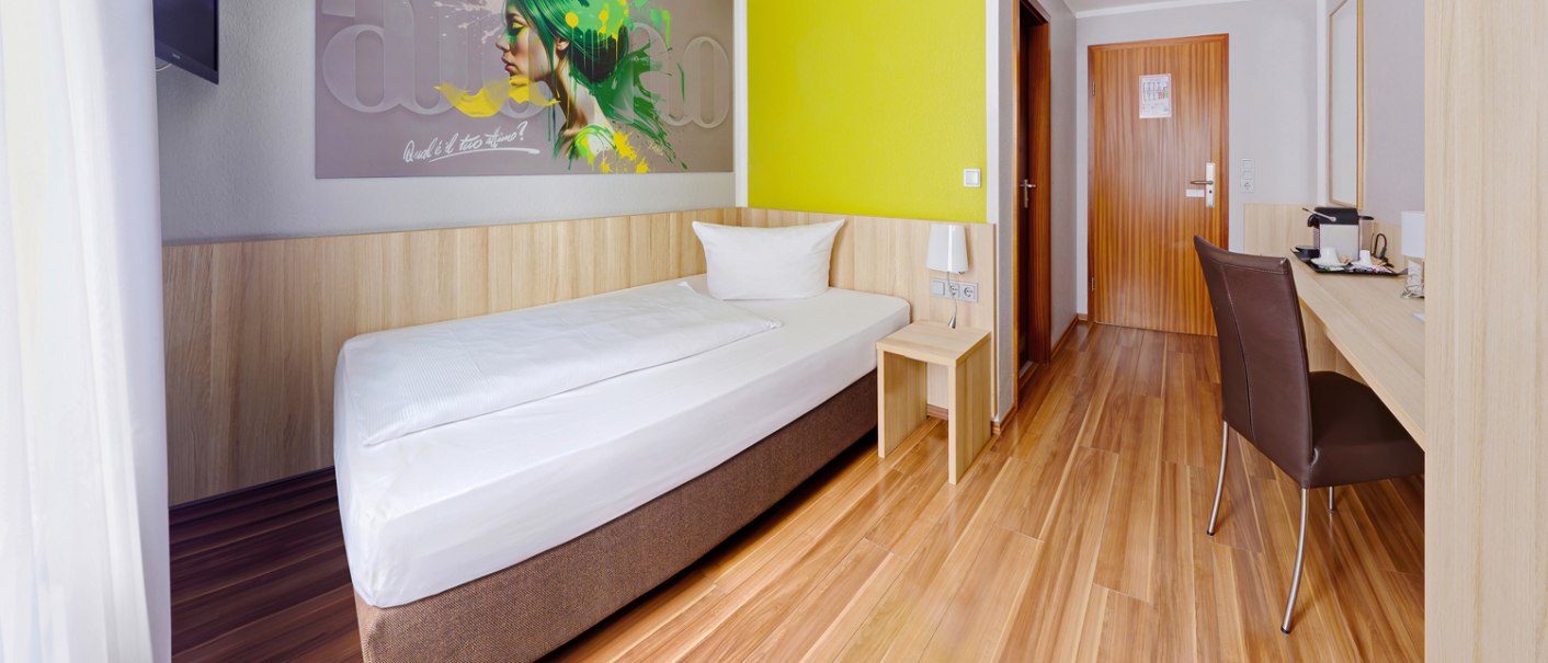 Modern single room with wooden floor, single bed, desk, wall art and yellow accent wall., © attimo Hotel Stuttgart Modern single room with wooden floor, single bed, desk, wall art and yellow accent wall., © attimo Hotel Stuttgart