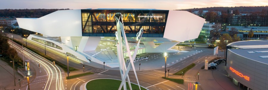 The Porsche Museum in Stuttgart at dusk, modern architecture with illuminated streets and a sculpture traffic circle in the foreground., © Porsche AG, Sabine Braun