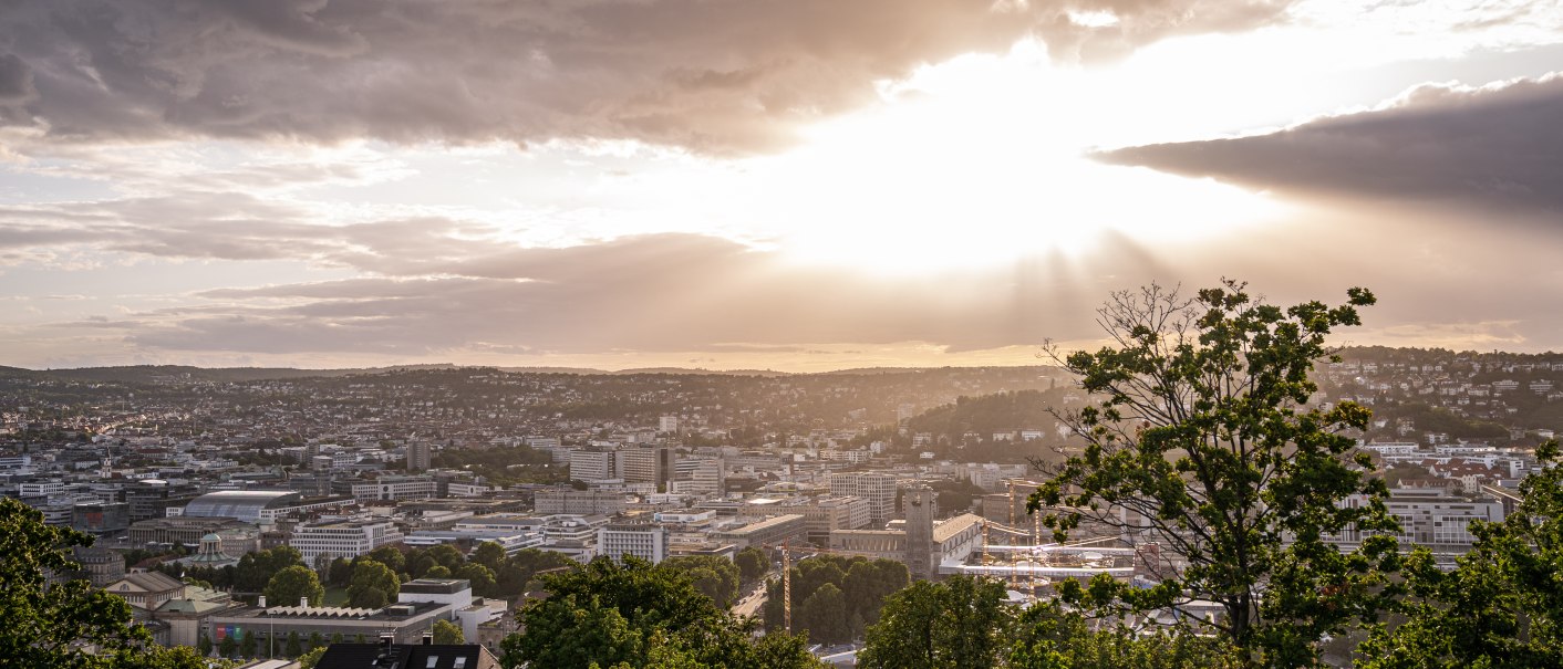 Sonnenuntergang über Stuttgart von der Uhlandshöhe aus. Die Stadt liegt unter einem bewölkten Himmel, durch den Sonnenstrahlen brechen., © Christine Garcia Urbina trickytine Sonnenuntergang über Stuttgart von der Uhlandshöhe aus. Die Stadt liegt unter einem bewölkten Himmel, durch den Sonnenstrahlen brechen., © Christine Garcia Urbina trickytine