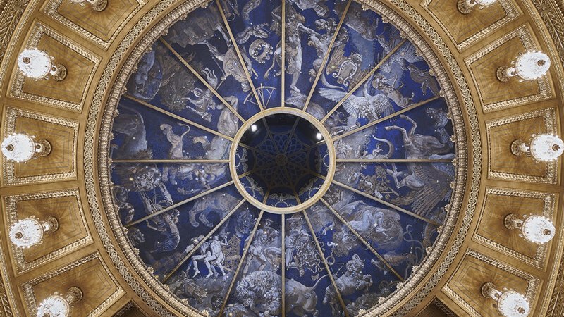 Prächtige Kuppeldecke mit blauen und goldenen Verzierungen, die Tierkreiszeichen darstellen. Elegante Beleuchtung umrahmt das kunstvolle Design., © Württembergische Staatstheater Stuttgart Prächtige Kuppeldecke mit blauen und goldenen Verzierungen, die Tierkreiszeichen darstellen. Elegante Beleuchtung umrahmt das kunstvolle Design., © Württembergische Staatstheater Stuttgart