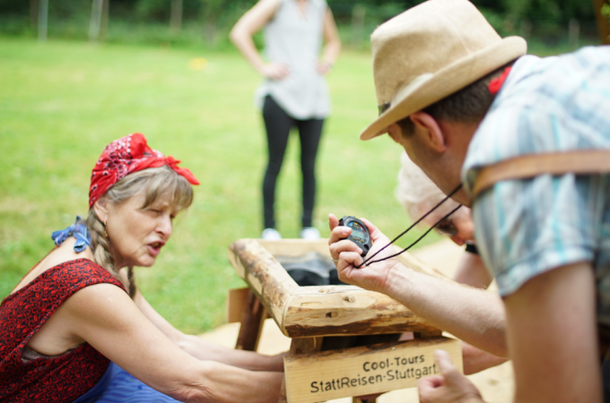 Eine Frau und ein Mann bei einer Outdoor-Aktivit&auml;t. Der Mann h&auml;lt eine Stoppuhr, die Frau arbeitet an einer Holzkonstruktion. Im Hintergrund eine weitere Person., &copy; Cool-Tours StattReisen