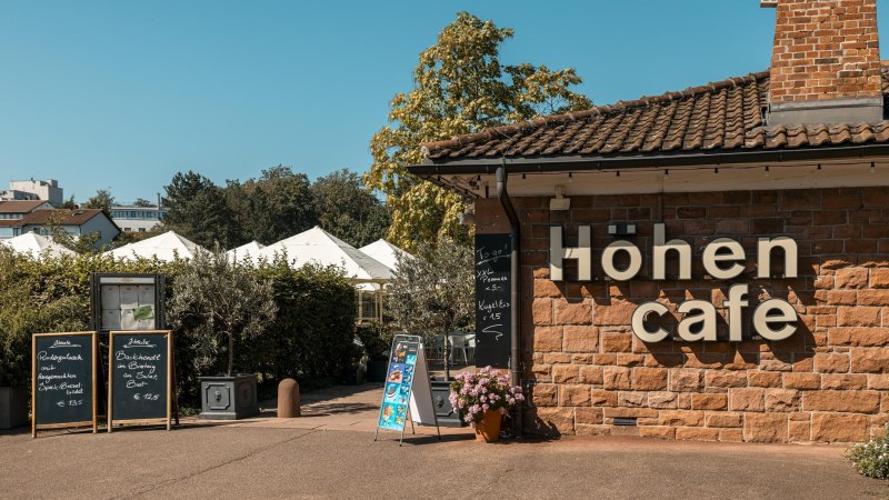 Das Höhen Café mit Schildern und Pflanzen im Außenbereich bei sonnigem Wetter., © SMG Stuttgart Marketing GmbH - Sarah Schmid