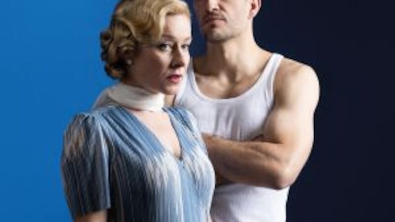 A woman in a blue dress and a man in a white undershirt stand in front of a two-tone background divided into blue and dark blue., © Altes Schauspielhaus und Komödie im Marquardt e.V. A woman in a blue dress and a man in a white undershirt stand in front of a two-tone background divided into blue and dark blue., © Altes Schauspielhaus und Komödie im Marquardt e.V.