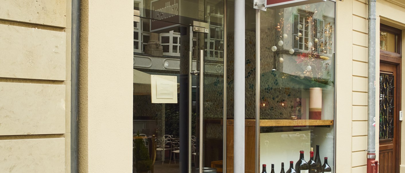 Eingang eines Geschäfts mit dem Schild 'Stadtbesen'. In der Vitrine stehen Weinflaschen. Eine rote Leuchtreklame ist an der Wand angebracht., © Stuttgart-Marketing GmbH, Sarah Schmid