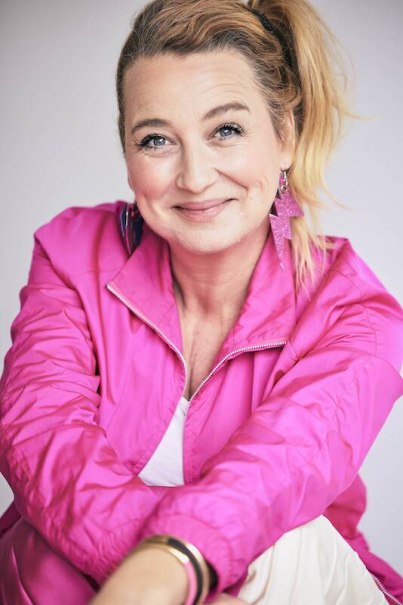A woman with blonde hair wears a pink jacket and smiles friendly into the camera. She has eye-catching earrings and bracelets., &copy; Rosenau Kultur e.V.