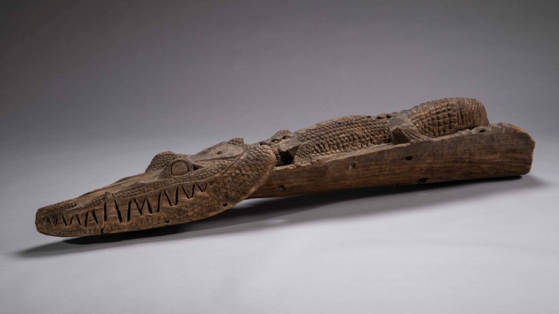 Holzskulptur eines Krokodils aus Papua-Neuguinea, detailreich geschnitzt mit markanten Zähnen und Schuppen. Liegt auf grauem Hintergrund., © Linden-Museum Stuttgart, Foto Dominik Drasdow Holzskulptur eines Krokodils aus Papua-Neuguinea, detailreich geschnitzt mit markanten Zähnen und Schuppen. Liegt auf grauem Hintergrund., © Linden-Museum Stuttgart, Foto Dominik Drasdow