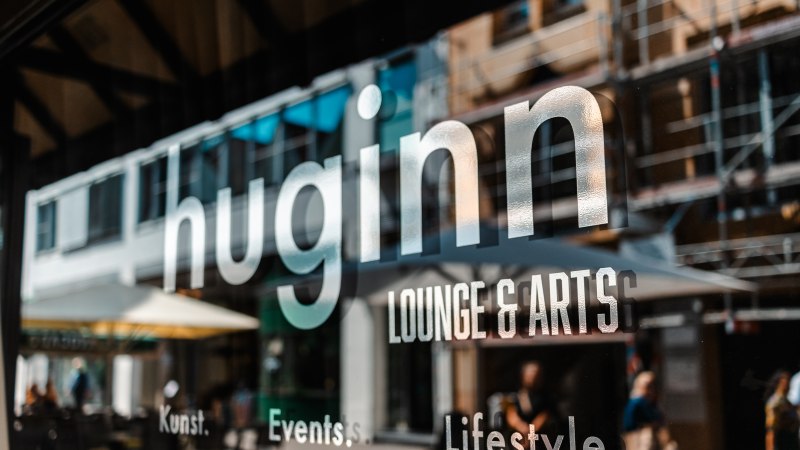 Schaufenster mit dem Schriftzug 'huginn LOUNGE & ARTS'. Im Hintergrund sind unscharf Menschen und Gebäude zu sehen., © SMG_Sarah Schmid
