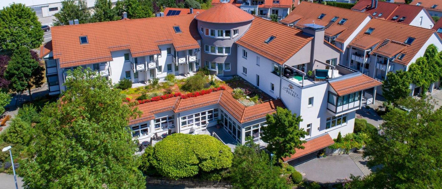 Das Hotel Landhaus Feckl zeigt eine Außenansicht mit roten Dächern, Balkonen und einem gepflegten Garten. Umgeben von Bäumen und einem gepflasterten Weg., © Landhaus Franz Feckl