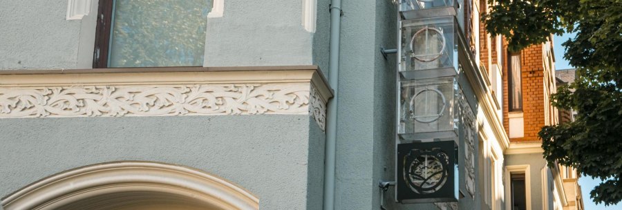 Facade of a building with decorated elements and a sign with logo. A tree casts shadows on the wall. Clear, sunny atmosphere., © SMG Stuttgart Marketing GmbH - Sarah Schmid