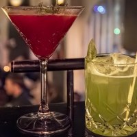 Two cocktails on a bar: a red one in a martini glass and a green one in a tumbler glass with a straw, blurred bar scene in the background., © SMG Stuttgart Marketing GmbH - Sarah Schmid Two cocktails on a bar: a red one in a martini glass and a green one in a tumbler glass with a straw, blurred bar scene in the background., © SMG Stuttgart Marketing GmbH - Sarah Schmid