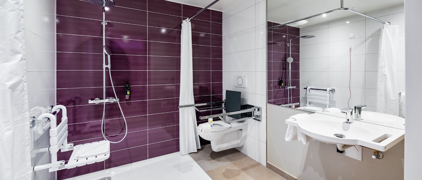 Modern, handicapped-accessible bathroom with purple tiles, grab rails, shower seat, WC and washbasin. Barrier-free equipment., © Premier Inn Modern, handicapped-accessible bathroom with purple tiles, grab rails, shower seat, WC and washbasin. Barrier-free equipment., © Premier Inn