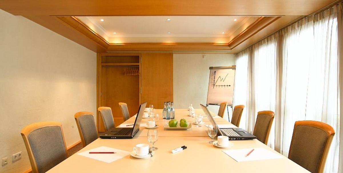 Konferenzraum mit Tisch, Stühlen, Laptops, Notizblöcken und Wasserflaschen. Flipchart mit Diagramm im Hintergrund, helle Vorhänge an den Fenstern., © Hotel am Park Konferenzraum mit Tisch, Stühlen, Laptops, Notizblöcken und Wasserflaschen. Flipchart mit Diagramm im Hintergrund, helle Vorhänge an den Fenstern., © Hotel am Park