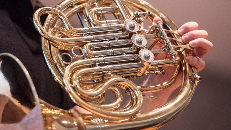 Nahaufnahme eines glänzenden Waldhorns, das von einer Person gespielt wird. Die Ventile und Röhren sind deutlich sichtbar., © Jens Volle Nahaufnahme eines glänzenden Waldhorns, das von einer Person gespielt wird. Die Ventile und Röhren sind deutlich sichtbar., © Jens Volle