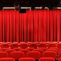 Empty theater hall with red chairs and closed red curtain, lighting and loudspeakers on the ceiling., © Sabine Haymann Empty theater hall with red chairs and closed red curtain, lighting and loudspeakers on the ceiling., © Sabine Haymann