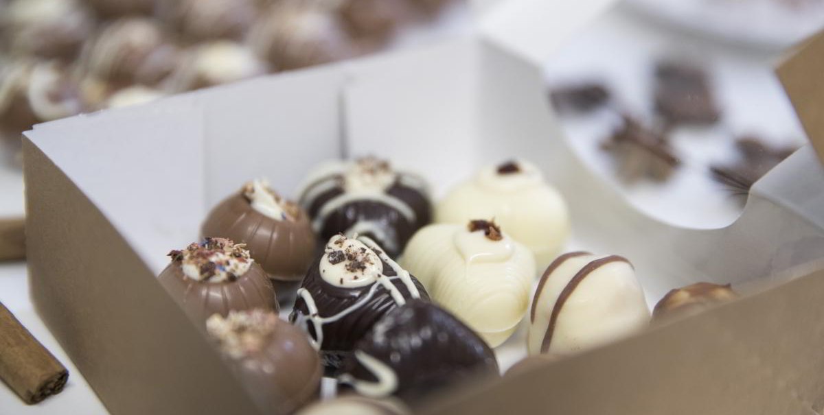 Eine Schachtel mit handgemachten Pralinen in verschiedenen Schokoladensorten, dekoriert mit Streuseln und Mustern., © hoponopo GmbH Eine Schachtel mit handgemachten Pralinen in verschiedenen Schokoladensorten, dekoriert mit Streuseln und Mustern., © hoponopo GmbH